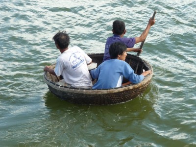 3 vissers in een gevlochten badkuipje, onderweg van de wal naar hun boot